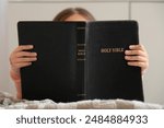 Cute little girl reading Bible at home, closeup