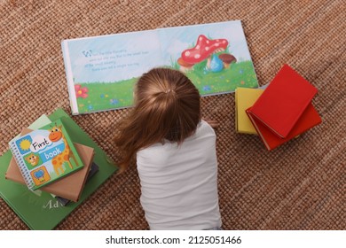 Cute little girl reading book on floor, top view - Powered by Shutterstock