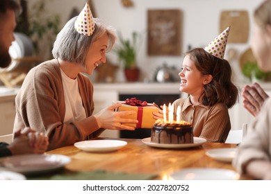 Cute Little Girl Receiving Congratulations From Grandma At Home, Loving Senior Woman Giving Gift To Excited Happy Granddaughter During Birthday Celebration With Family, Cake With Candles On Table