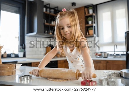 Cute little girl rolling the dough with a rolling pin to make sugar cookies