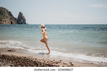 Cute little girl running along the seashore against a clear blue sea and rejoices in the rays of the summer sun. Beautiful girl in yellow swimsuit running and having fun on tropical beach. - Shutterstock ID 2256048627