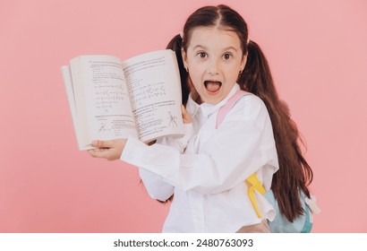 Cute little girl in school uniform with backpack with shocked face and open mouth holding math book and showing equation on pink background - Powered by Shutterstock