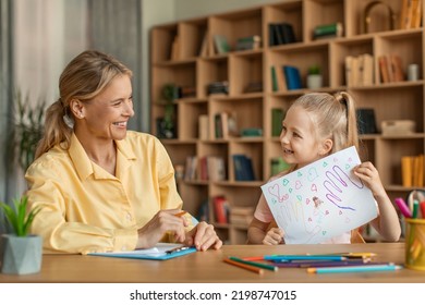 Cute Little Girl Showing Attractive Woman Psychologist Her Drawing, Kid Having Therapy Session With Child Development Specialist At Clinic