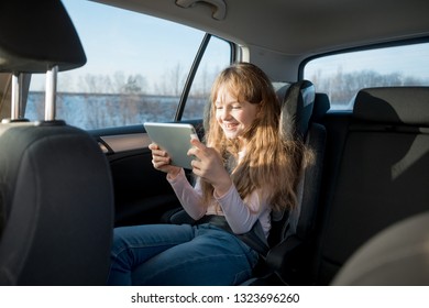 Cute Little Girl Sitting In Child Car Seat Playing On Tablet And Having Fun