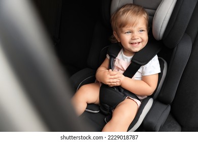 Niña pequeña y educada sentada en un asiento de seguridad infantil dentro del auto