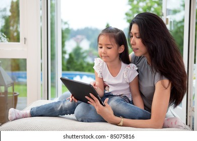 Cute little girl sitting with her mother on couch using a digital tablet