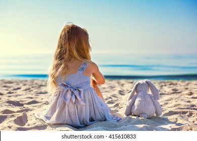 Cute Little Girl Sitting At Ocean Beach. Back View