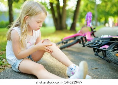 Cute little girl sitting on the ground after falling off her bike at summer park. Child getting hurt while riding a bicycle. Active family leisure with kids.
