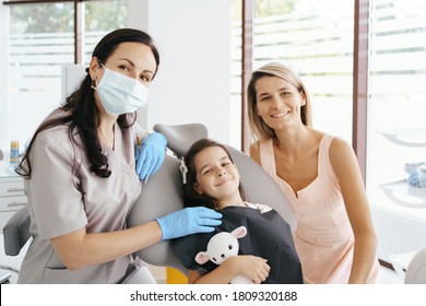 Cute Little Girl Sitting On A Modern Dental Chair With Mom And Having Dental Consultation With Dentist