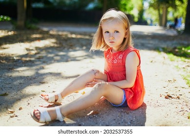 Cute Little Girl Sitting On The Ground After Falling Down. Child Getting Hurt While Walking In Park. Kid Looking At Her Boo-boo