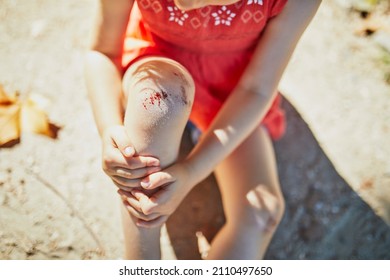 Cute Little Girl Sitting On The Ground After Falling Down. Child Getting Hurt While Walking In Park. Kid Looking At Her Boo-boo