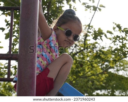 Cute little girl sitting in swinging.Wearing indian pink dress.Black eyeglass with different pose portrait photo.Using for ai editing and wallpaper also.