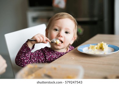 Cute Little Girl Sitting At The Table Eating Mashed Potatoes