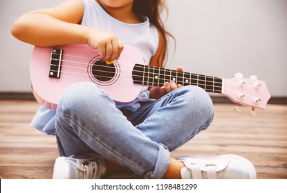 Cute little girl in smart fashiony clothes playing pink ukulele sitting on floor - Powered by Shutterstock