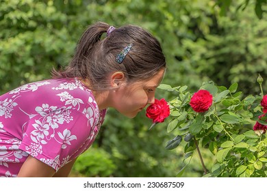 Cute little girl smelling red rose in the garden with green bokeh.