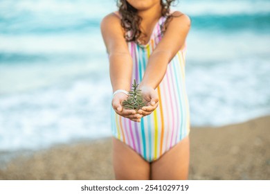 Cute little girl standing on the beach in Santa hat and striped swimsuit and smiling. Kid holding Christmas tree toy in miniature. Christmas tropical vacation concept - Powered by Shutterstock