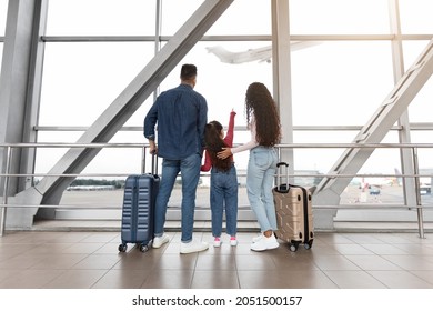 Cute Little Girl Standing With Parents In Airport Terminal, Looking At Plane Out Of Window, Rear View. Middle Eastern Family Of Three Waiting For Flight Boarding, Ready For Vacation Travel Together