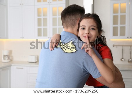 Cute little girl sticking paper fish to father's back at home Photo stock © 
