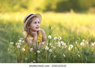 Cute Little Girl In A Straw Hat Has Sits On A Summer Field With Dandelions. Child Having Activity Fun Outside. Concept Of A Healthy Child Without Allergies. High Quality Photo. High Quality Photo