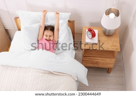 Cute little girl stretching in cosy bedroom, above view