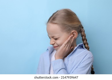 Cute Little Girl Suffering From Ear Pain On Light Blue Background