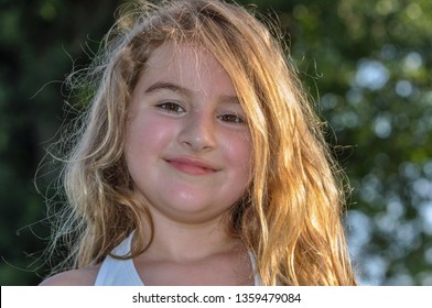 Cute Little Girl With A Sunburnt Face. Red Hot Sweaty Face. A Little Girl With A Sun Burnt Face And Sunburnt Lips. A Small Child With Sweat On Her Face.  Golden Hour Sunlight Puts A Backlight On Hair.