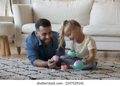 Cute Little Girl Takes Care Of Her Loving Daddy Pours Imaginary Tea Into Cup From Toy Teapot, Play Together In Modern Warm Living Room On Weekend Use Plastic Toy Dishware. Family Playtime, Fun Concept