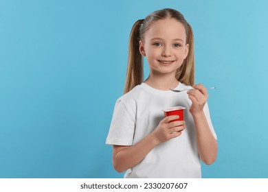Cute little girl with tasty yogurt on light blue background, space for text
