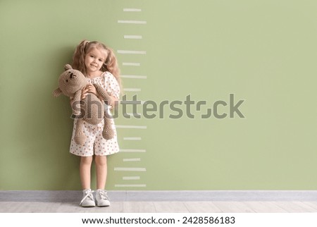 Cute little girl with toy measuring height near green wall