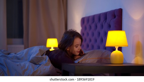 Cute Little Girl Turning Off Bed Lamp And Falling Asleep In Bed. Side View Of Adorable Preteen Kid Lying In Bed At Bedtime And Sleeping. Happy Child In Bed Late In Evening