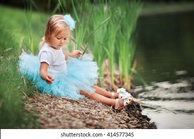 Cute little girl in turquoise tutu skirt sitting near the river and playing with pebbles. Adorable kid enjoying the nature. Fashion child joying in green summer park.