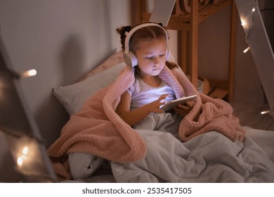 Cute little girl using tablet computer in bedroom at night - Powered by Shutterstock