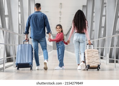 Cute Little Girl Walking With Parents Together In Airport Terminal, Shappy Middle Eastern Family Carrying Luggage And Holding Hands, Adorable Female Child Turning At Camera, Ready For Vacation Travel