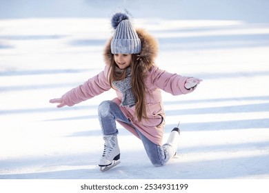 Cute little girl in warm pink coat, grey knitted hat and scarf, snood learning to skate on ice skating rink in park. Fall down and have fun. Winter sport, outdoors. Holiday and seasonal concept.