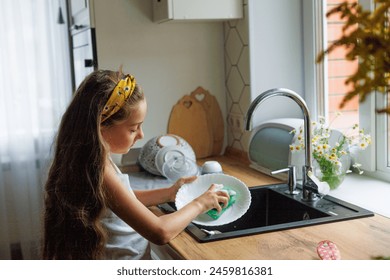 Cute little girl washing dishes with sponge in kitchen sink at home. Child doing chores concept. - Powered by Shutterstock