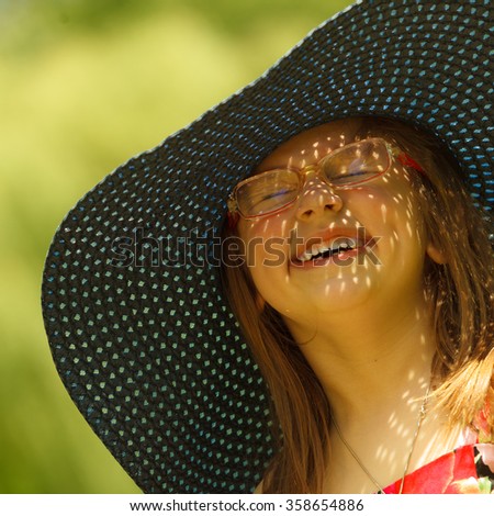 Cute little girl wearing big summer hat pretending to be woman lady. Child imitate mother playing in park, outdoors