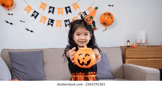 Cute little girl wearing a Halloween costume holding a pumpkin at home with happy eyes. looking at the camera.