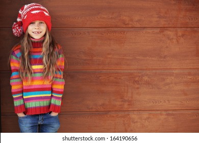 Cute little girl wearing knit winter clothes posing over wooden background