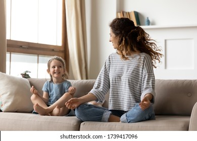 Cute Little Girl Wearing Princess Diadem With Young Mother Sitting In Lotus Pose On Cozy Couch At Home, Mum And Adorable Daughter Practicing Yoga Together, Family Having Fun On Weekend