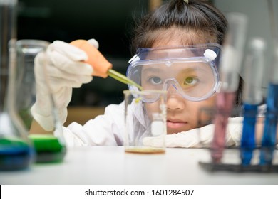 Cute little girl wearing safty goggle and lab coat making experiment in chemical laboratory, ecucation and science concept - Powered by Shutterstock