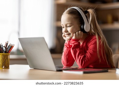 Cute Little Girl Wearing Wireless Headphones Study At Home With Laptop, Smiling Preteen Female Child Looking At Computer Screen, Watching Online Lesson, Enjoying Remote Education, Free Space - Powered by Shutterstock