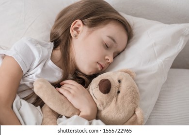 Cute little girl in a white bed sleeping with a soft toy . The concept of children's sleep and development .