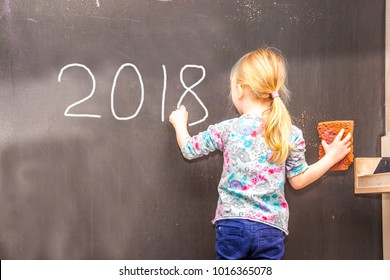 Cute little girl writing 2018 on chalkboard in a classroom