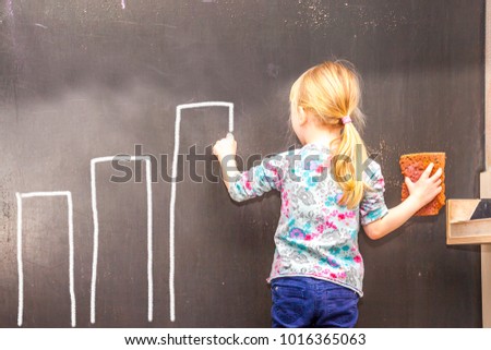 Cute little girl writing bars on chalkboard in a classroom