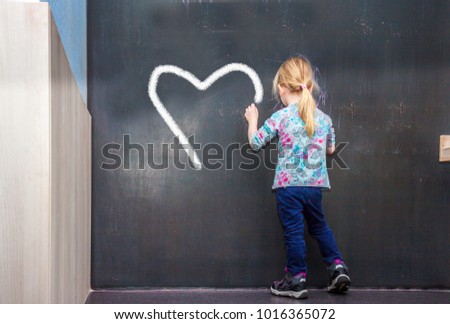 Cute little girl writing a heart on chalkboard in a classroom