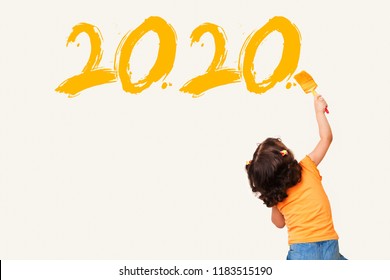 Cute little girl writing new year 2020 with painting brush on wall background
