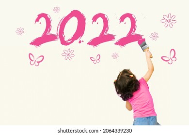 Cute little girl writing new year 2022 with pink painting brush on wall background