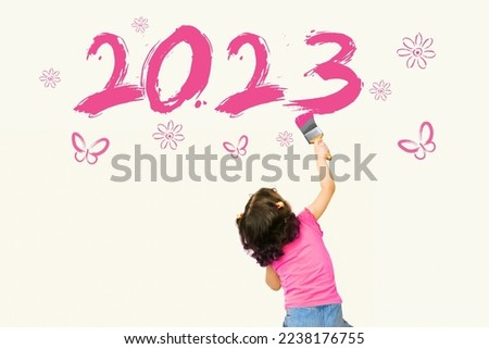Cute little girl writing new year 2023 using painting brush on wall background