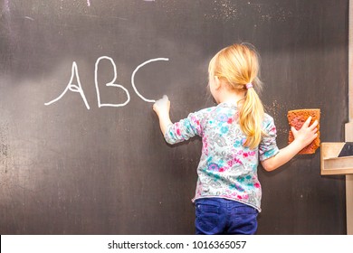 Cute little girl writing on chalkboard in a classroom