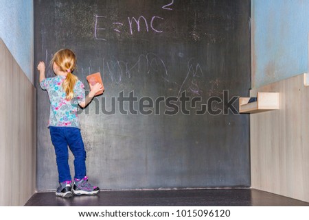 Cute little girl writing on chalkboard in a classroom